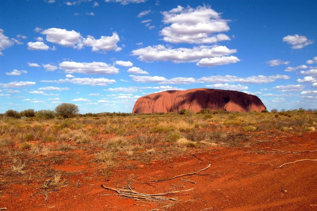Een foto van Uluru (Ayers Rock) in het rode hart van Australië, omringd door droge outback-vegetatie