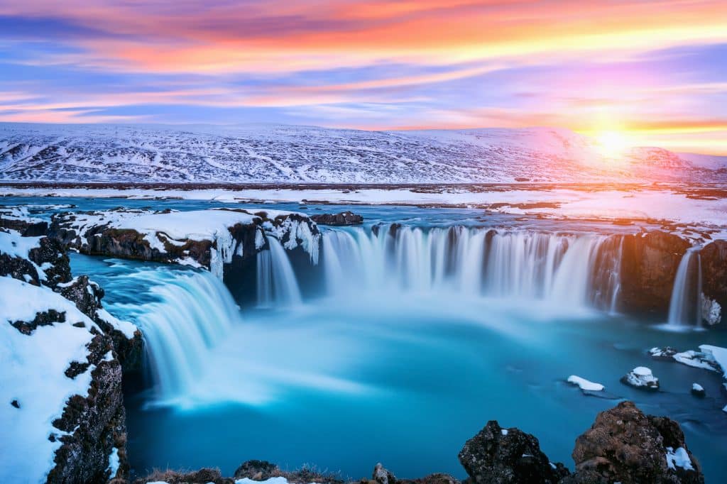 Een foto van de Godafoss waterval in IJsland, omgeven door sneeuw en kleurrijke lucht