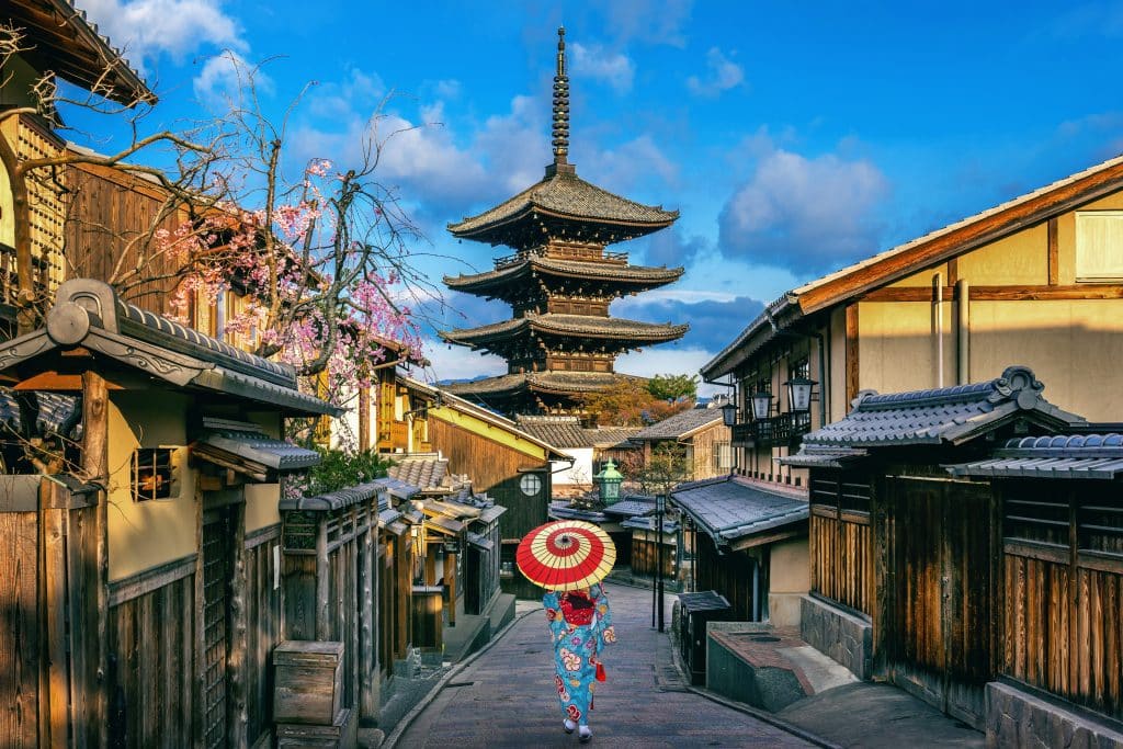 Een foto van de Yasaka-pagode in Kyoto, met een vrouw in kimono die onder een rode parasol loopt
