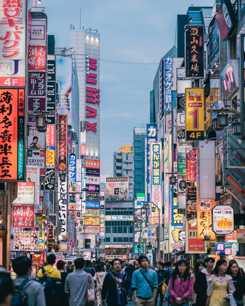 Een foto van een drukke winkelstraat in Tokio, met felle neonlichten en talloze mensen