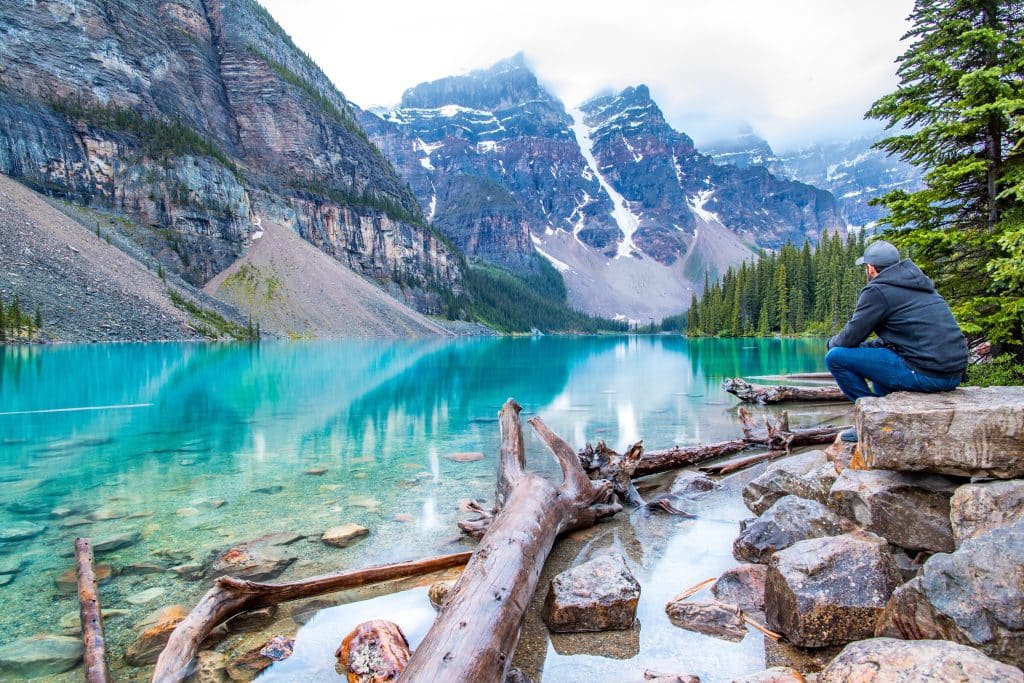 Man zit tijdens de Western Canada Explorer aan helderblauw meer met bergen in Canada